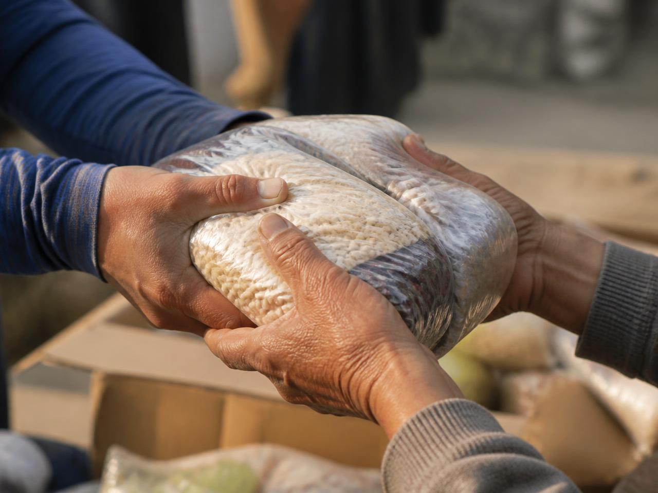Hands passing a parcel of food supplies to another pair of hands in warm daylight